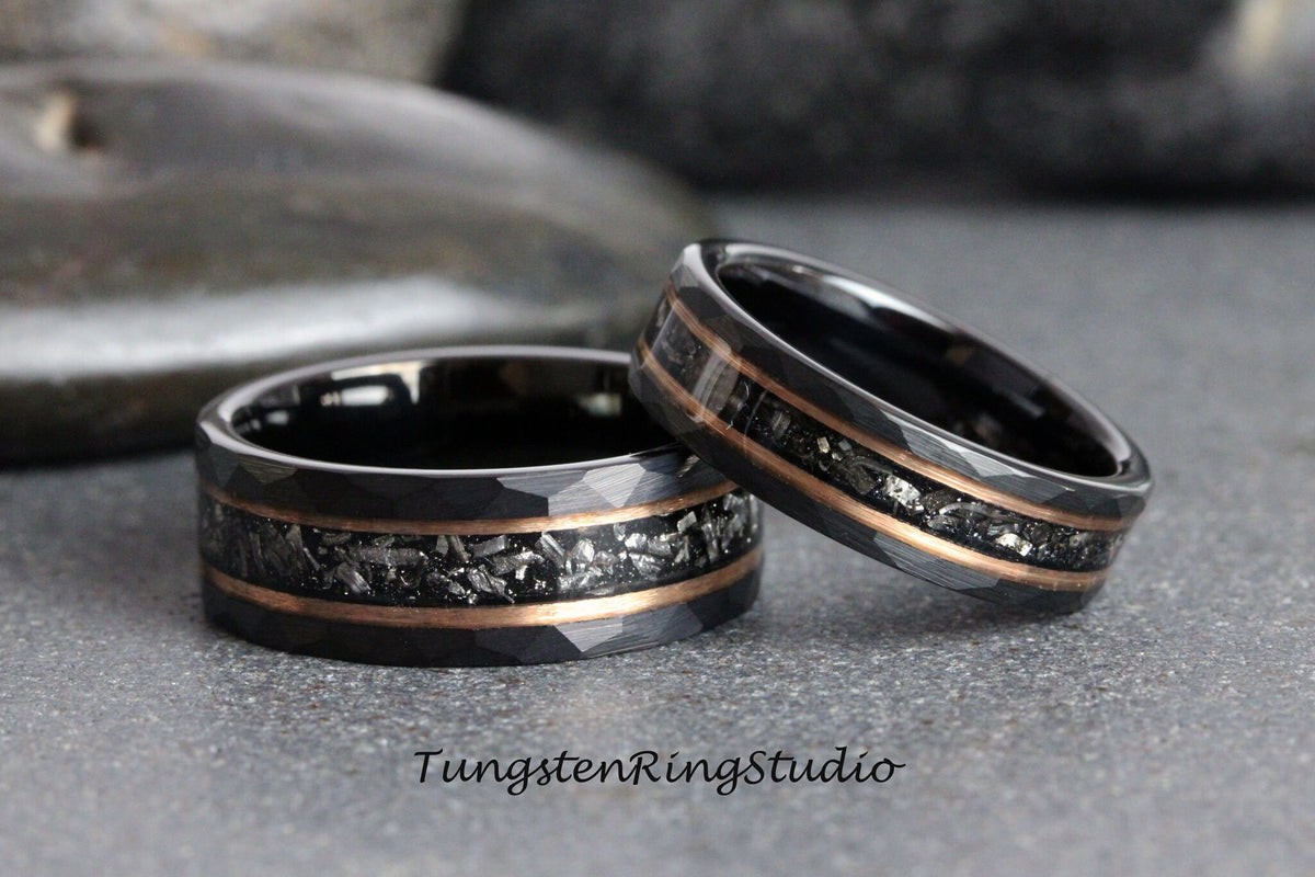 May include: Two black tungsten carbide rings with a rose gold inlay and a meteorite-like pattern. The rings are stacked on top of each other.