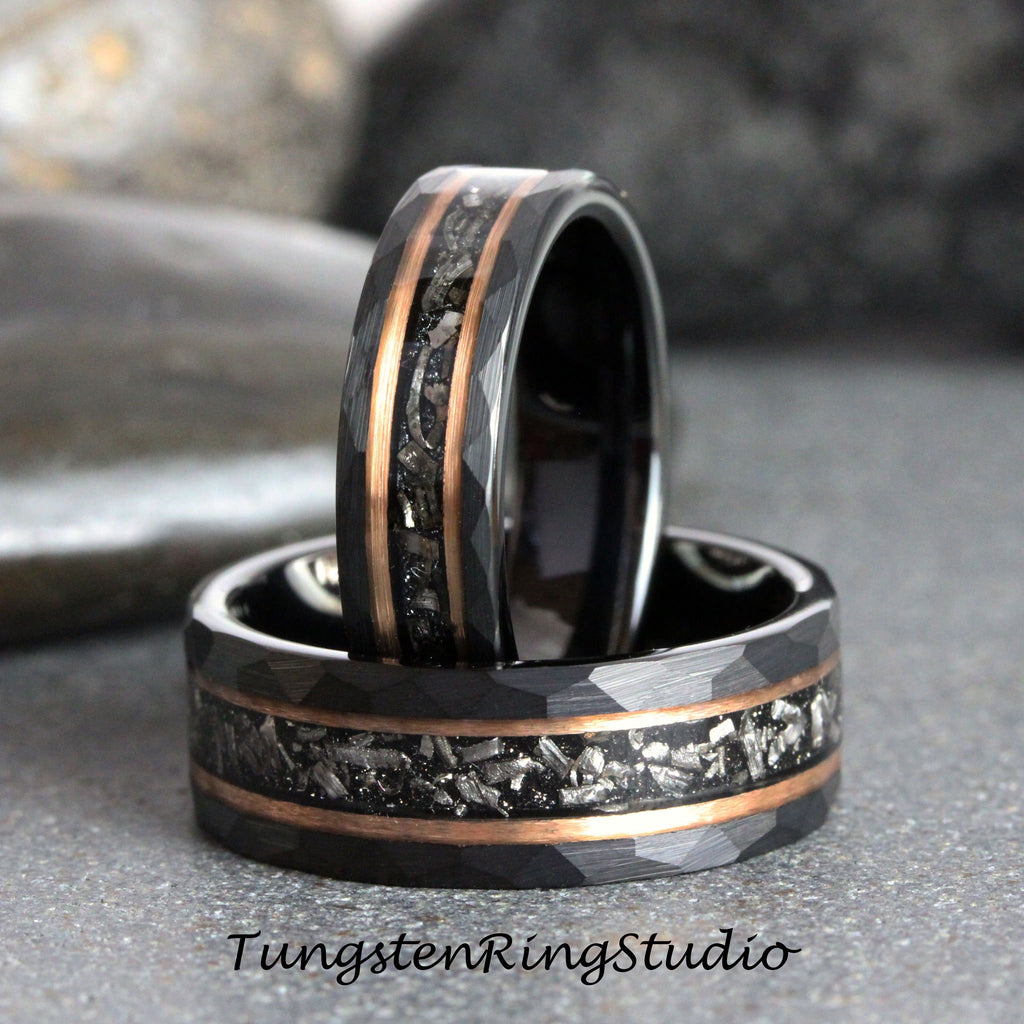 May include: Two black tungsten carbide rings with a hammered finish and a rose gold inlay. The inlay features a pattern of small, silver-colored particles.