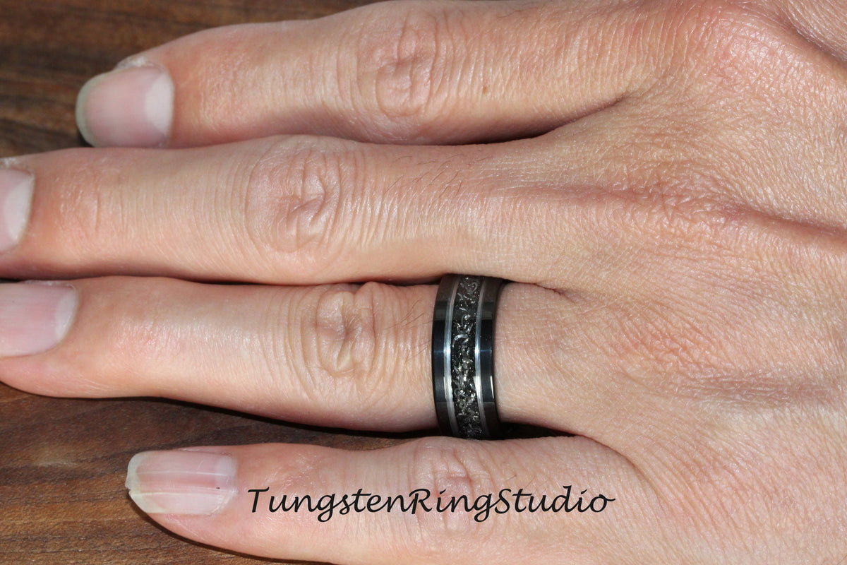 May include: A black tungsten carbide ring with a black and silver patterned design. Tungsten Ring Studio.