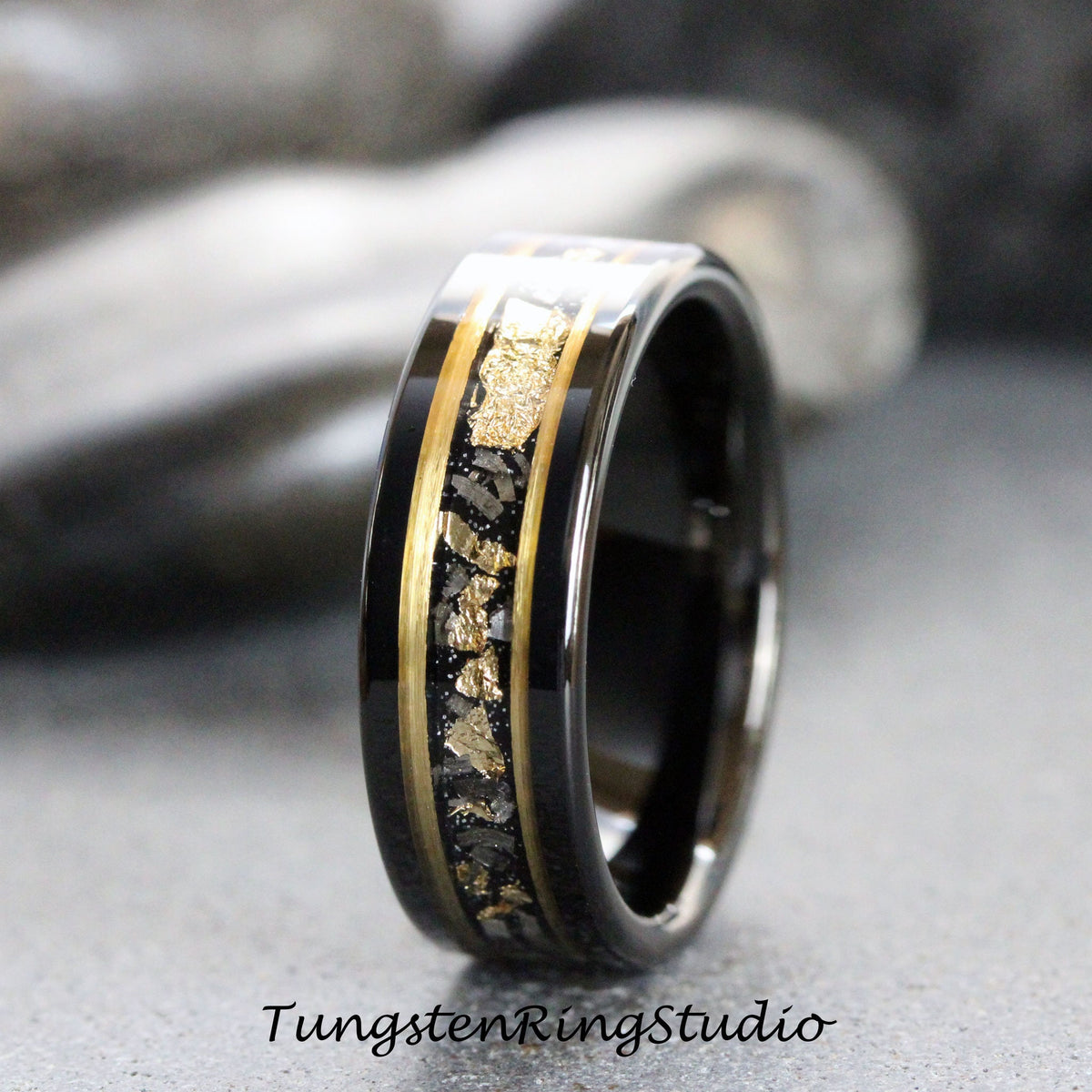 May include: A black tungsten carbide ring with a gold inlay featuring a pattern of small gold flakes. The ring has a polished finish.