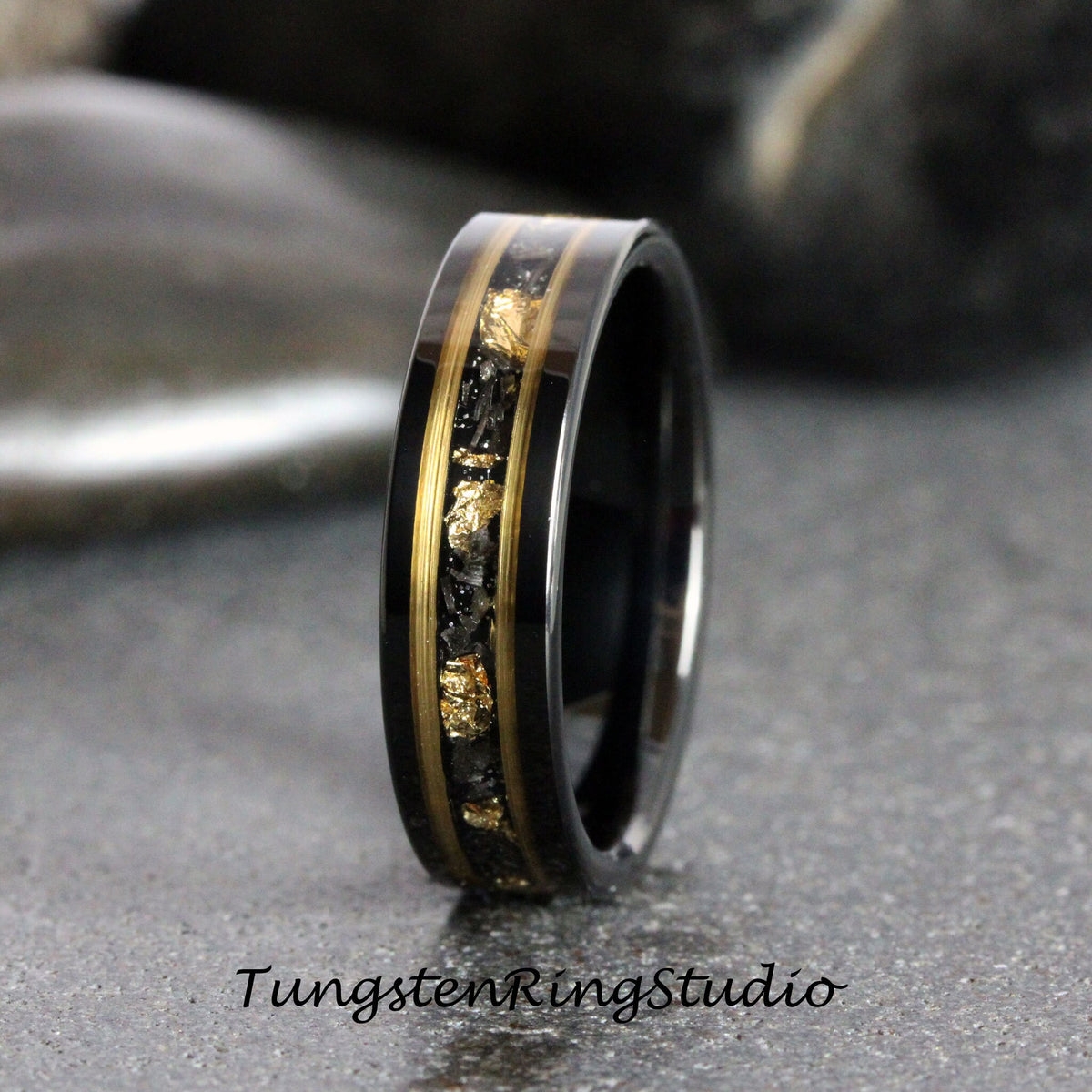 May include: A black tungsten carbide ring with a gold inlay featuring a pattern of small gold flakes. The ring has a polished finish.