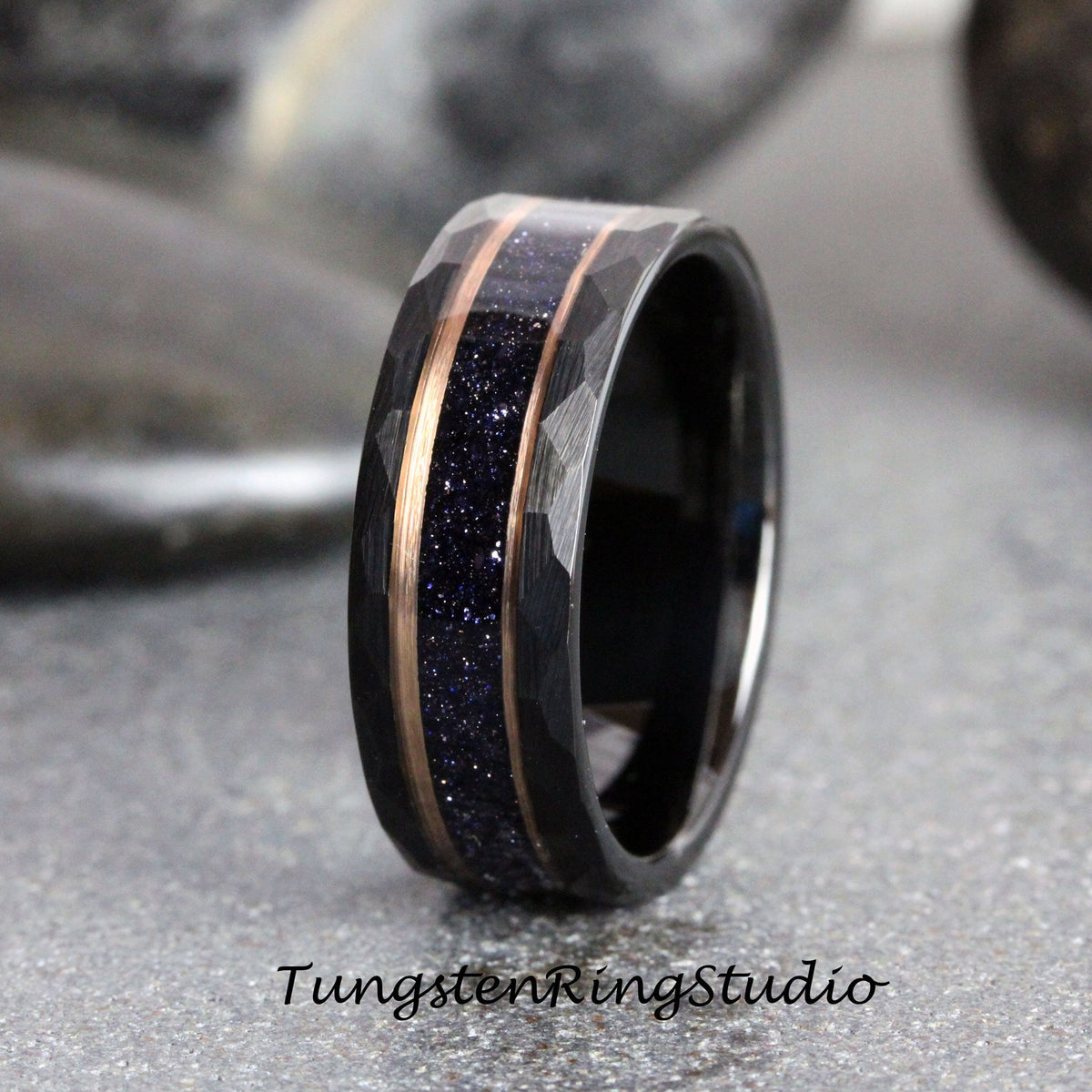 May include: A black tungsten carbide ring with a hammered finish and a rose gold inlay. The inlay features a band of blue glitter.