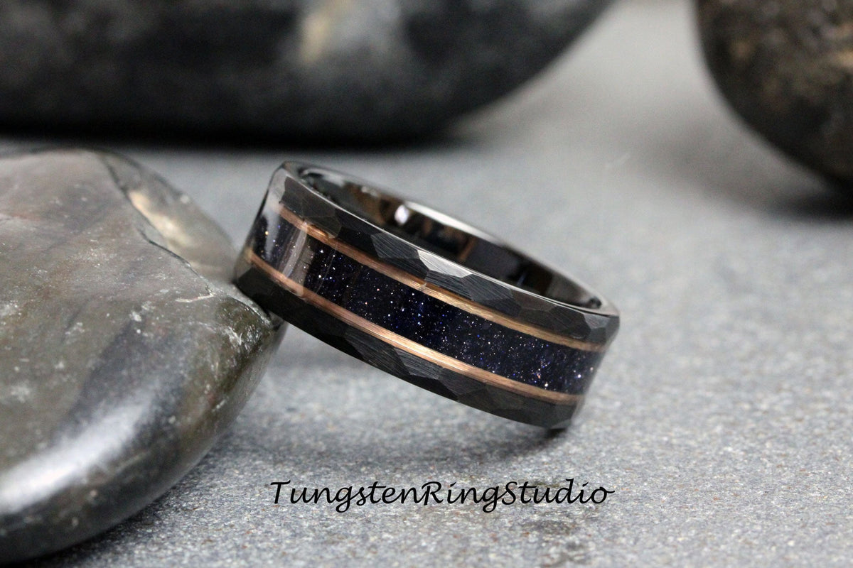 May include: A black tungsten ring with a hammered finish and two rose gold inlays. The inlays are filled with blue glitter.