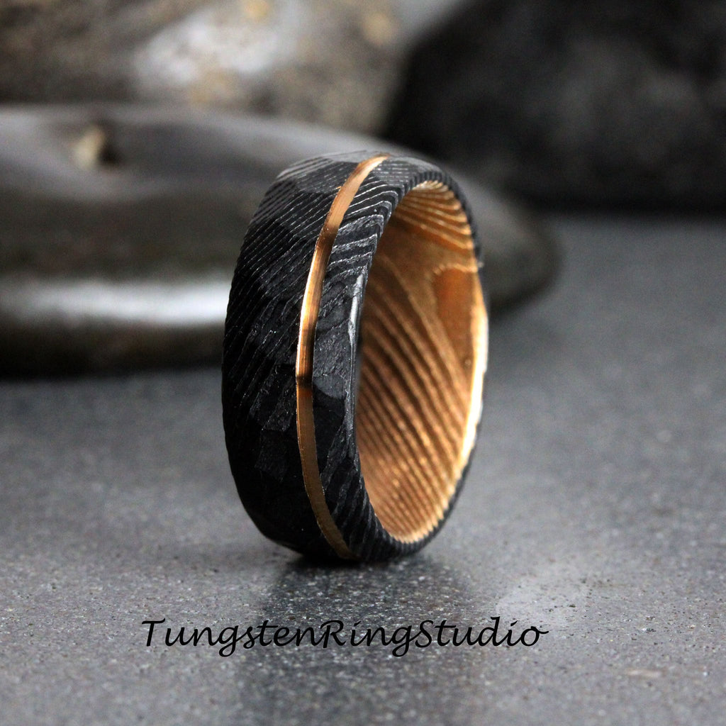 May include: A black and gold tungsten carbide ring with a wood inlay. The ring has a hammered finish and a thin gold band around the center.