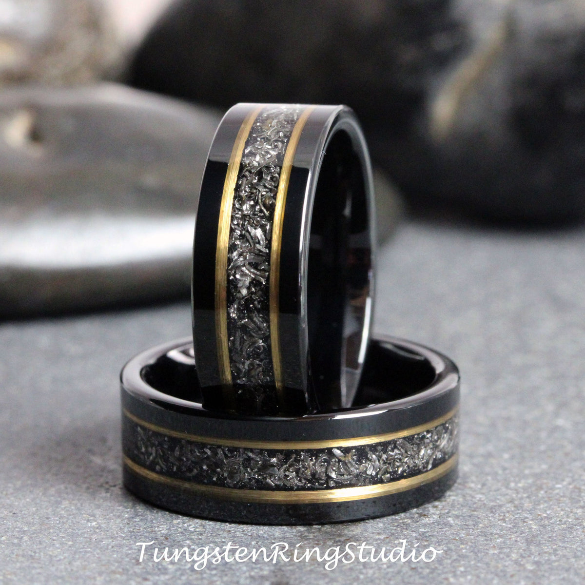 May include: Two black tungsten carbide rings with a gold inlay and a silver fleck design. The rings are stacked on top of each other.