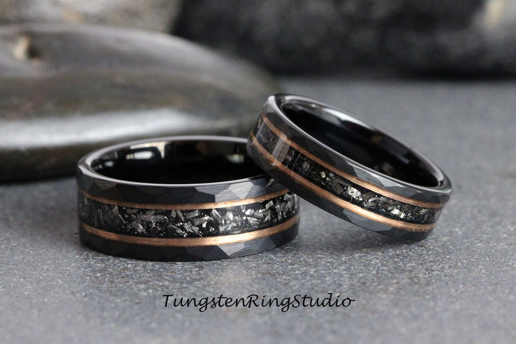 May include: Two black tungsten carbide rings with a rose gold inlay and a meteorite-like pattern. The rings are stacked on top of each other.