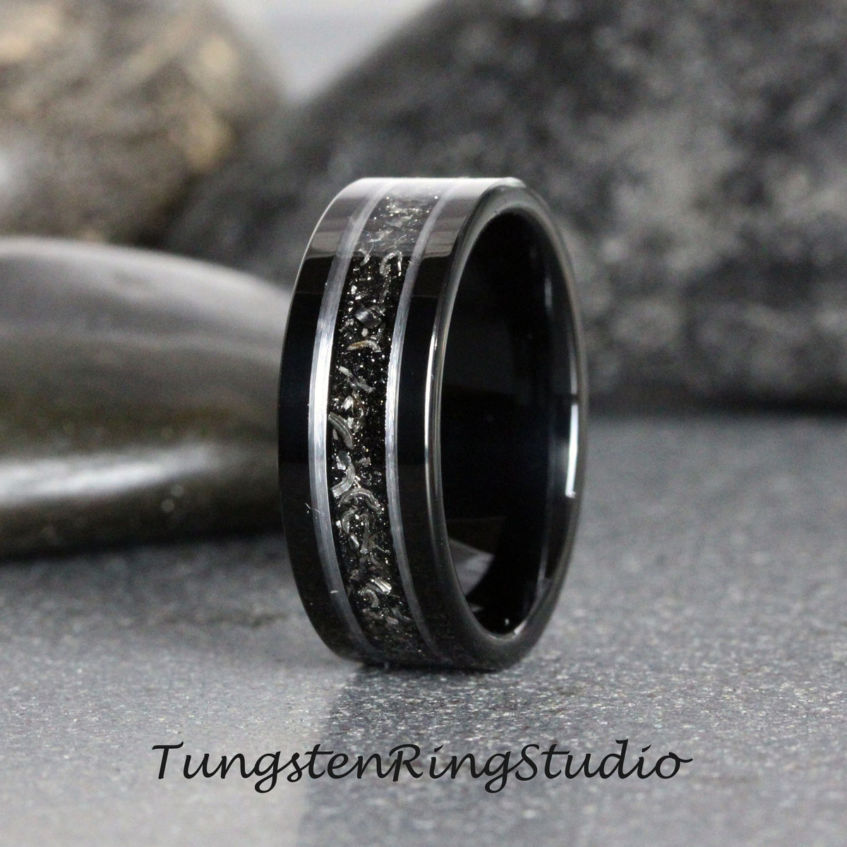 May include: A black tungsten carbide ring with a silver inlay. The inlay has a textured, speckled pattern. The ring is polished and has a beveled edge.