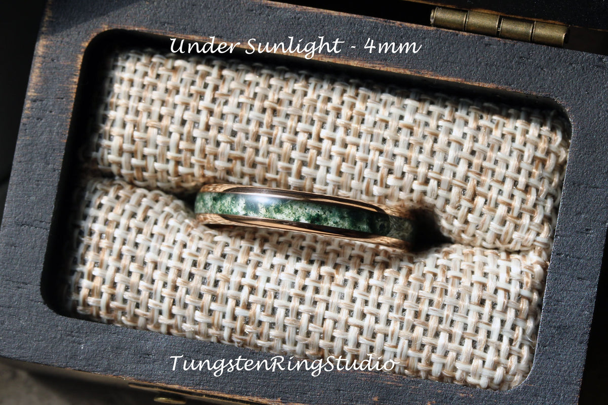 May include: A green and gold tungsten ring with a green stone inlay, in a small wooden box with a beige fabric lining. The text "Under Sunlight - 4mm" is visible above the ring. The text "TungstenRingStudio" is visible below the ring.