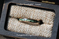 May include: A green and gold tungsten ring with a green stone inlay, in a small wooden box with a beige fabric lining. The text "Under Sunlight - 4mm" is visible above the ring. The text "TungstenRingStudio" is visible below the ring.