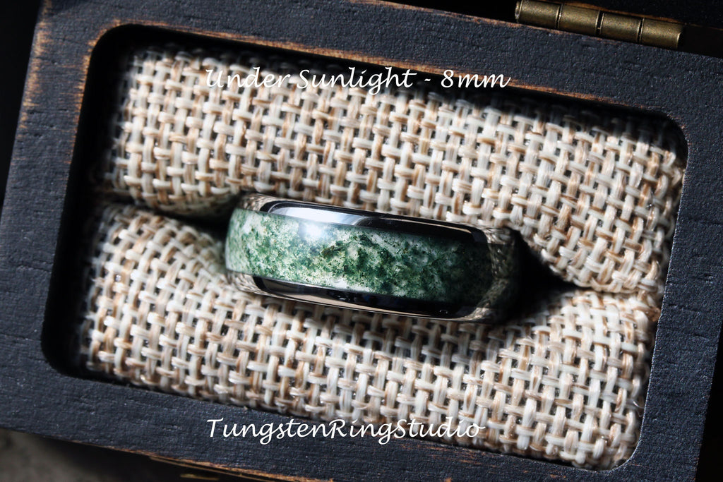 May include: A tungsten ring with a green agate inlay. The ring is 8mm wide and is displayed in a wooden box with a fabric lining. The text "under sunlight - 8mm" and "TungstenRingStudio" are visible in the image.