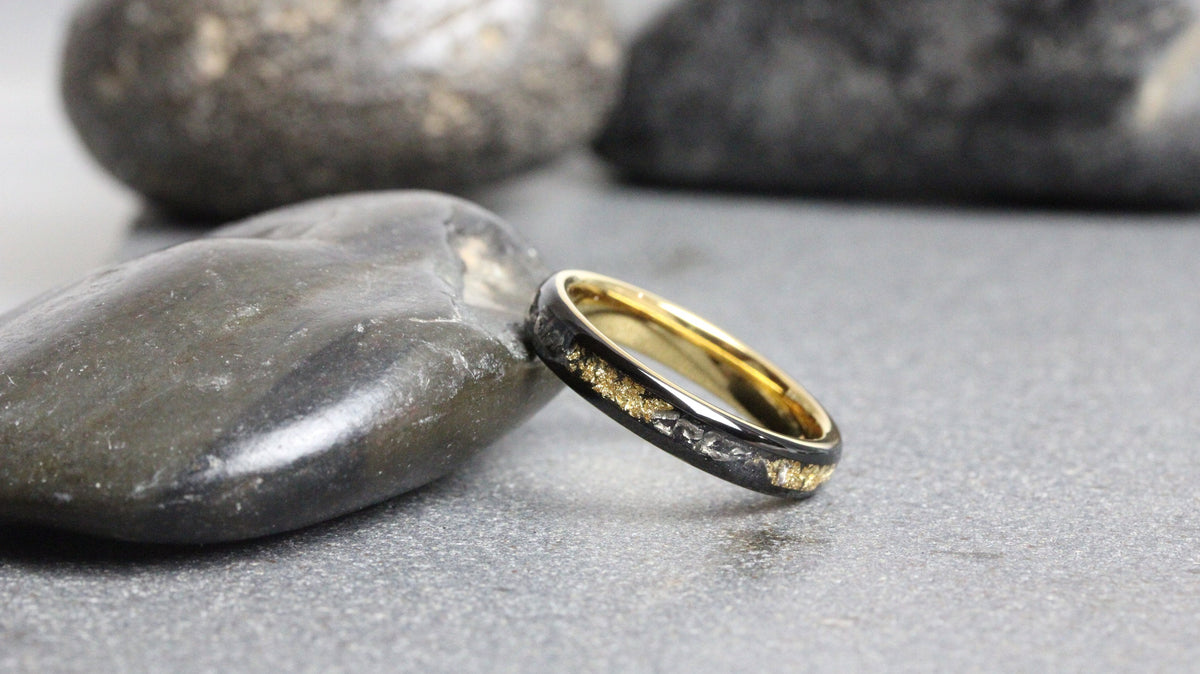 May include: A black and gold wedding band with a thin gold band and a black band with a gold inlay.