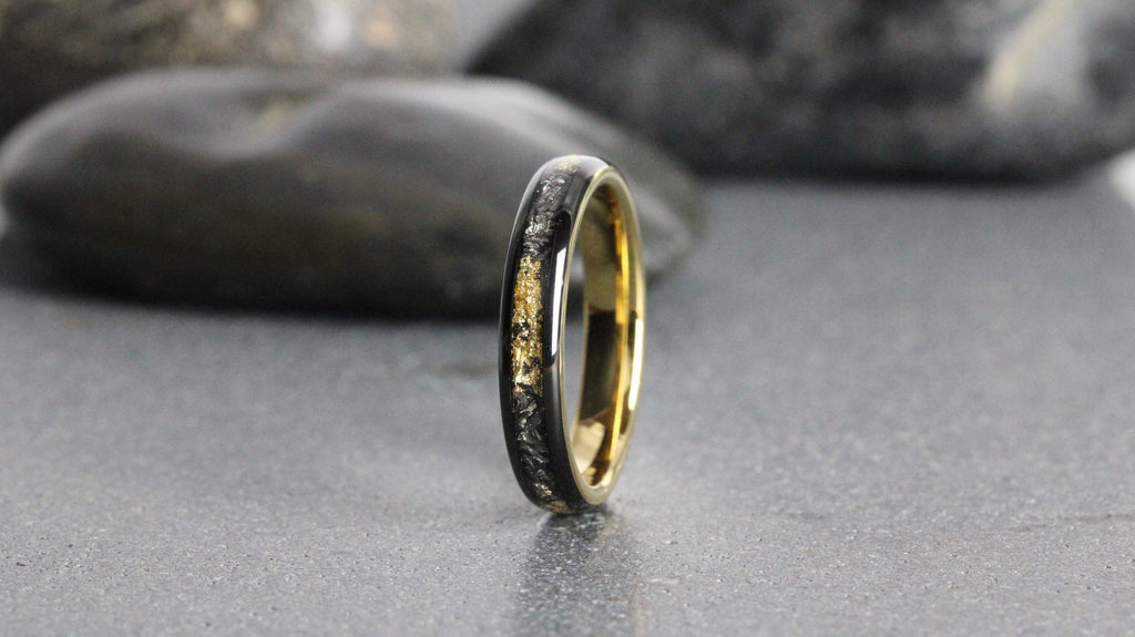 May include: A black and gold wedding band with a thin gold band and a black band with gold flecks.