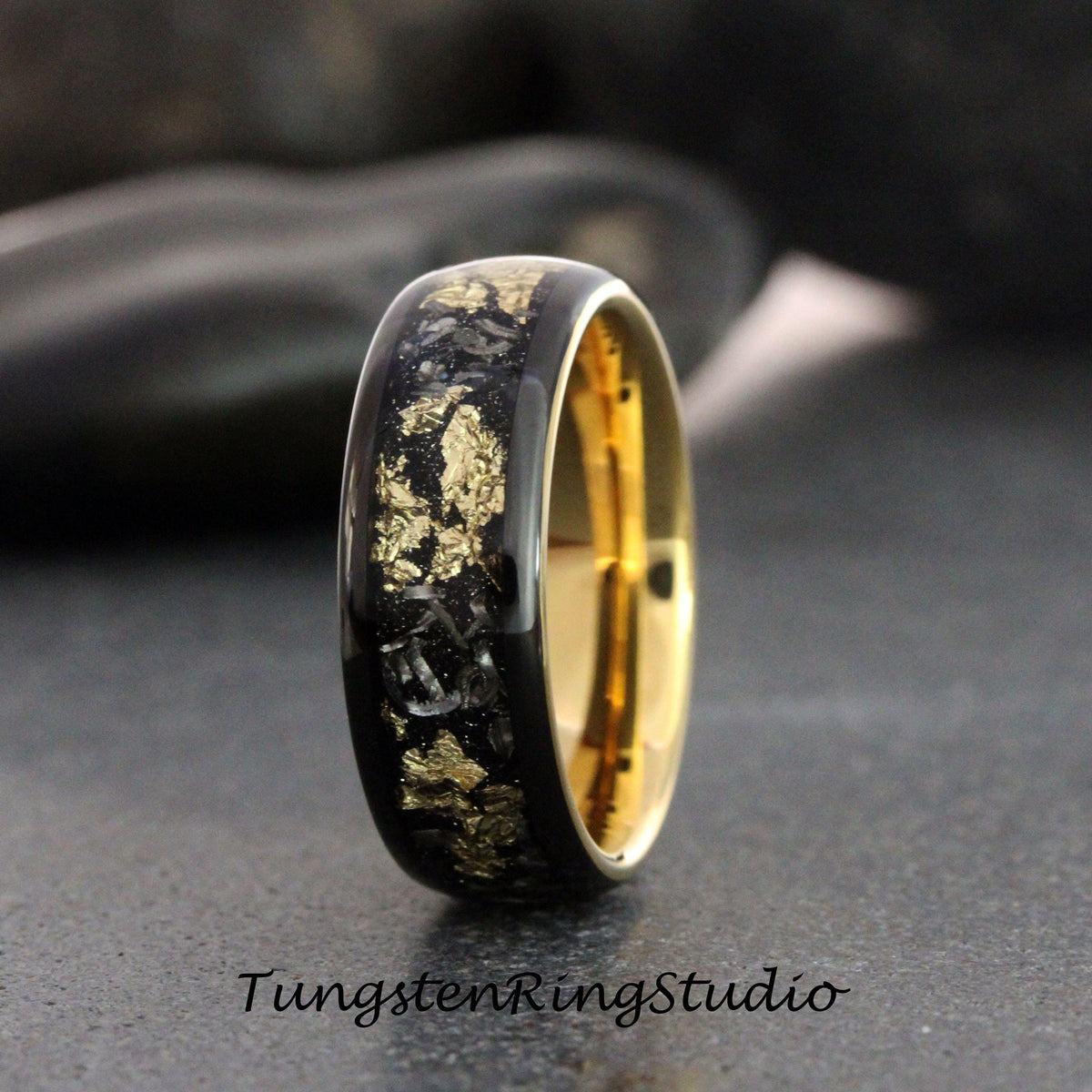 May include: A black tungsten carbide ring with a gold inlay. The inlay is made of gold flakes and is arranged in a pattern. The ring is polished and has a high shine.