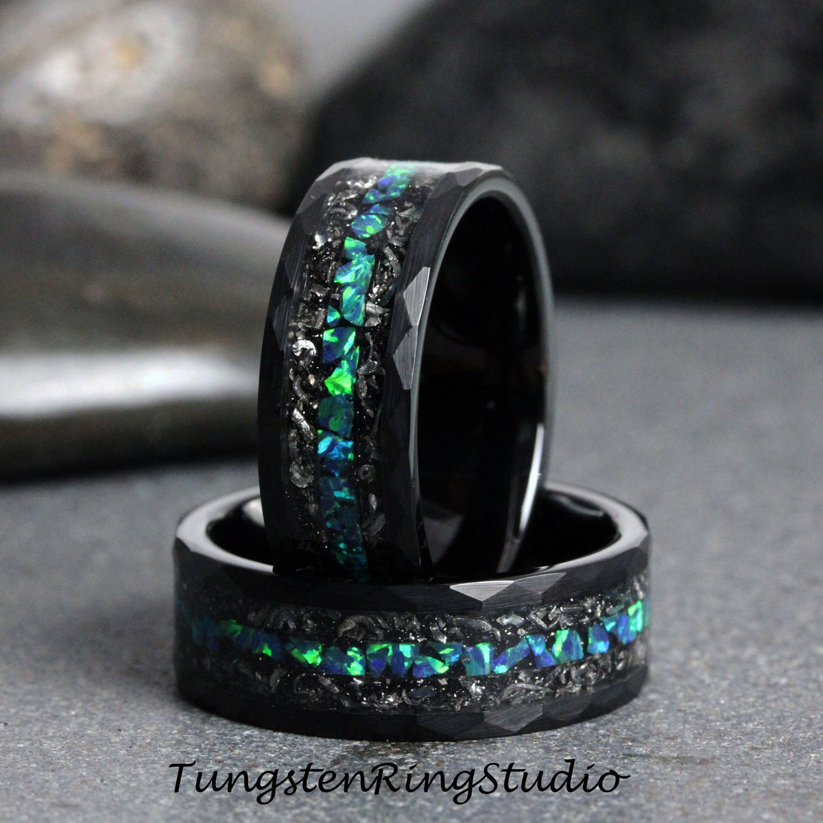 May include: Two black tungsten carbide rings with a green and blue opal inlay. The rings have a hammered finish and are stacked on top of each other.