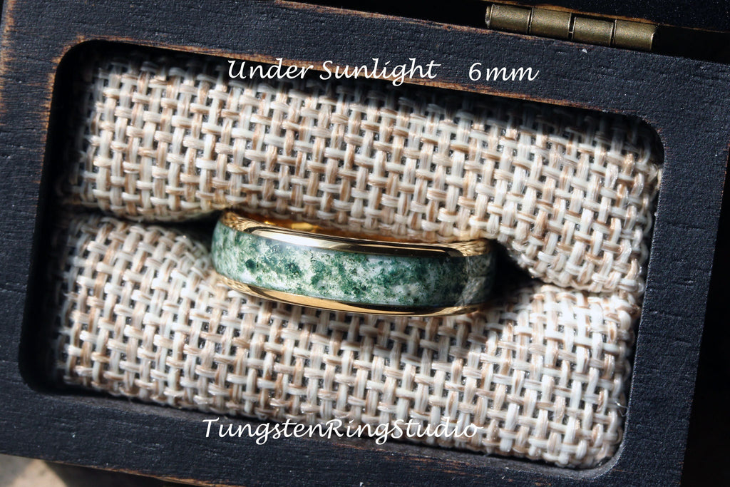 May include: A green and gold tungsten ring with a green stone inlay. The ring is 6mm wide and is displayed in a wooden box. "Under Sunlight" and "TungstenRingStudio" are printed on the box.