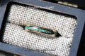 May include: A gold tungsten ring with a green stone inlay. The ring is in a small wooden box with a brown fabric lining. The text "Under Sunlight" is printed on the box. The text "TungstenRingstudio" is printed on the bottom of the box.