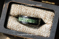 May include: A black tungsten ring with a green inlay and beveled edges. The ring is 8mm wide and is displayed in a wooden box with a burlap lining. The text "Under Sunlight - 8mm" is visible on the box.