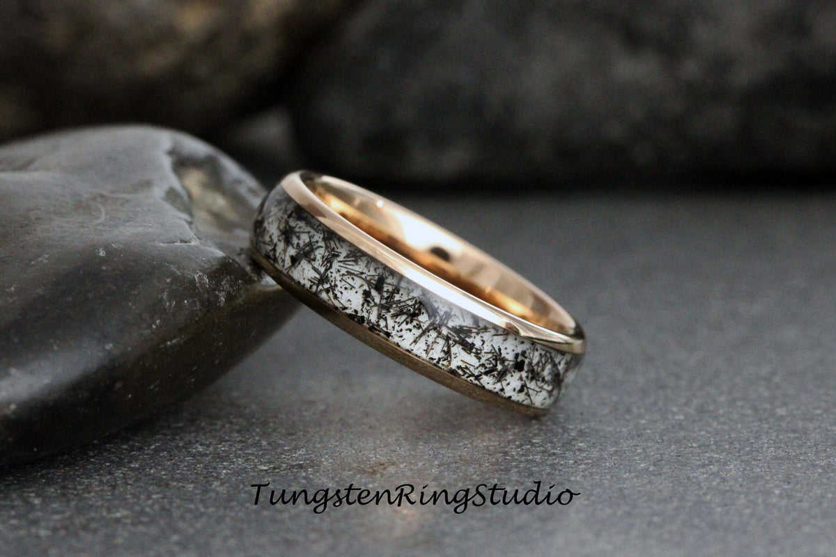 May include: A black and white tungsten carbide ring with a rose gold band. The ring has a unique, speckled pattern.
