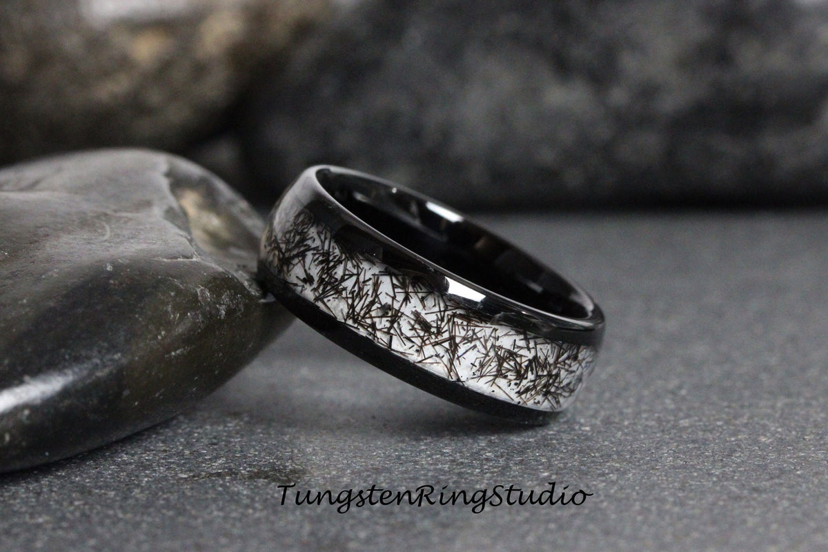 May include: A black tungsten ring with a white inlay featuring a unique pattern of black lines. TungstenRingStudio is printed on the background.