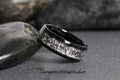 May include: A black tungsten ring with a white inlay featuring a unique pattern of black lines. TungstenRingStudio is printed on the surface below the ring.