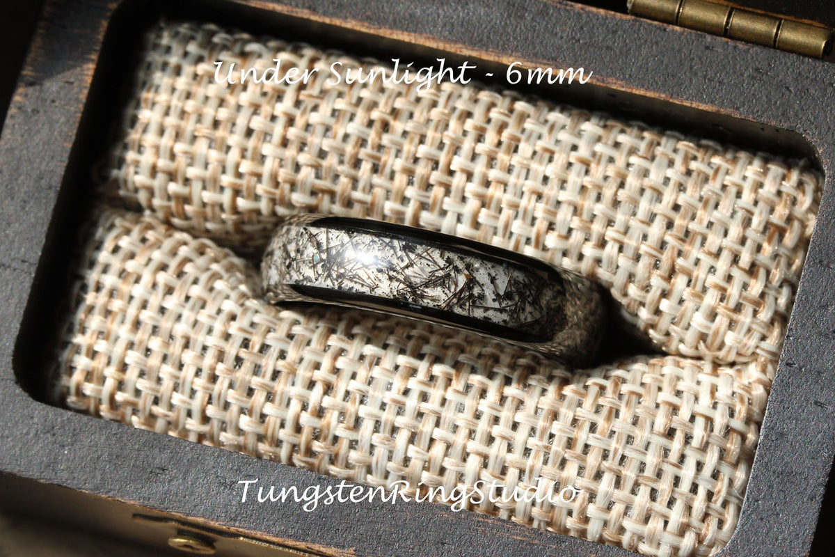 May include: A black tungsten carbide ring with a white and black meteorite inlay. The ring is 6mm wide and is displayed in a wooden box with a fabric lining. The text "Under Sunlight - 6mm" is visible above the ring.