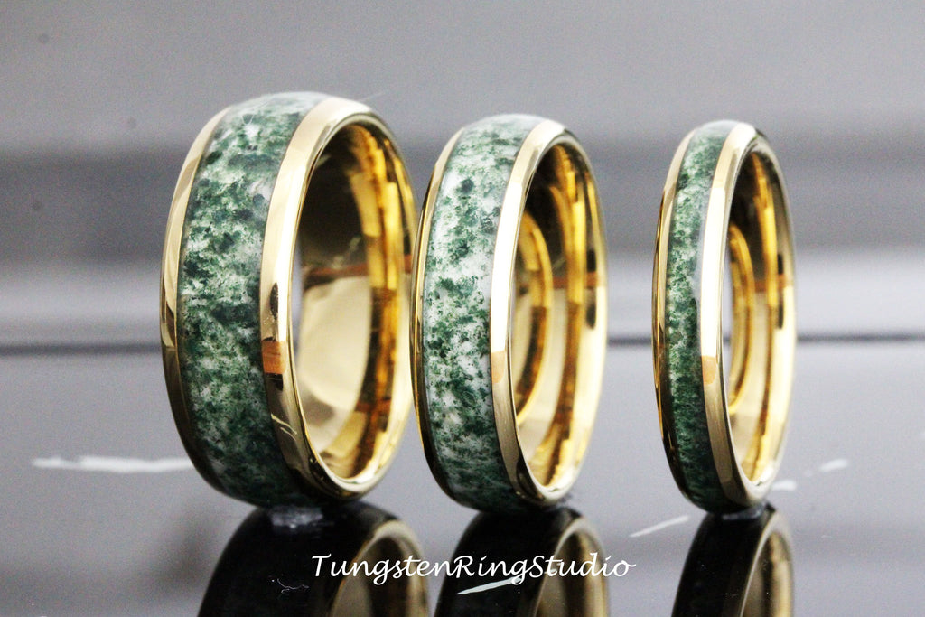 May include: Three tungsten carbide rings with a gold inlay and green stone inlay. The rings are different sizes.