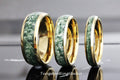 May include: Three tungsten carbide rings with a gold inlay and green stone inlay. The rings are different sizes.