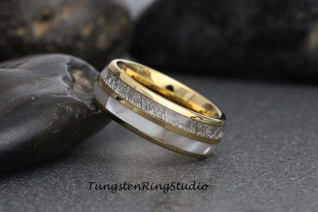 May include: A gold and silver tungsten carbide ring with a white mother-of-pearl inlay. The ring has a brushed finish and a beveled edge.