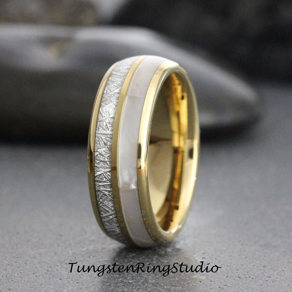 May include: A gold and silver tungsten carbide ring with a white inlay. The ring has a brushed finish and a beveled edge.