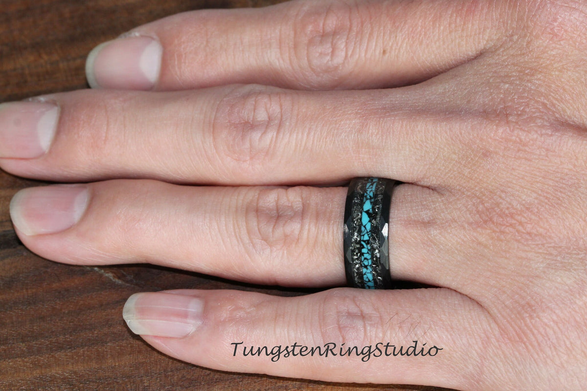 May include: A black tungsten ring with a turquoise inlay and a black carbon fiber band. The ring is worn on a person's finger.