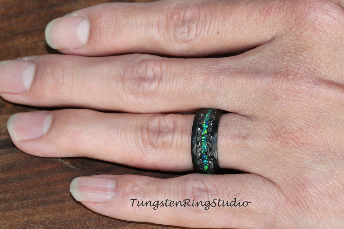 May include: A black tungsten ring with a green and black inlay. The ring is on a person's finger.
