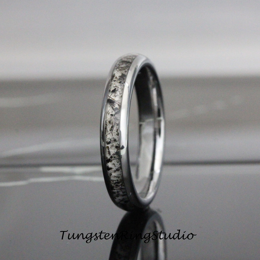 May include: A silver tungsten carbide ring with a black and white meteorite inlay. The ring is polished and has a beveled edge.