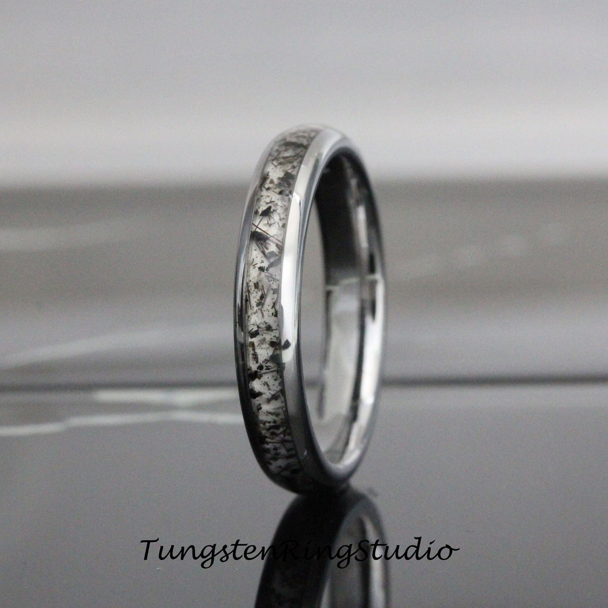 May include: A silver tungsten carbide ring with a black and white meteorite inlay. The ring is polished and has a beveled edge.