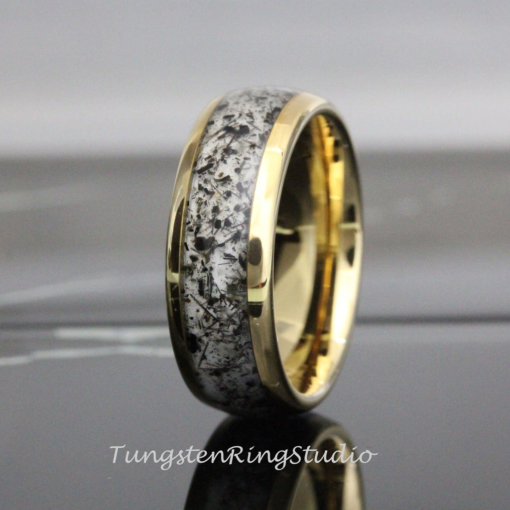 May include: A gold-colored ring with a band of white and black speckled material. The ring has a polished finish and a smooth, rounded shape. The text "TungstenRingStudio" is visible at the bottom of the image.