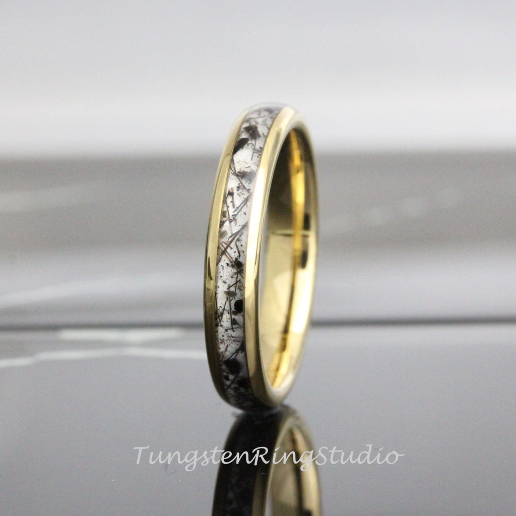 May include: A gold-colored ring with a band of white and black speckled material. The ring has a polished, reflective surface. The text "TungstenRingStudio" is visible at the bottom of the image.