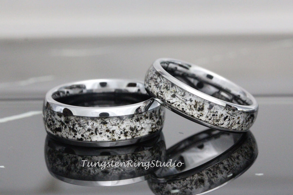 May include: Two silver tungsten carbide rings with a black and white speckled design. The rings have a beveled edge.