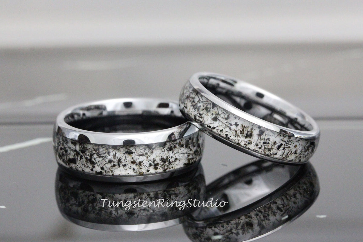 May include: Two silver tungsten carbide rings with a black and white speckled design. The rings have a beveled edge.