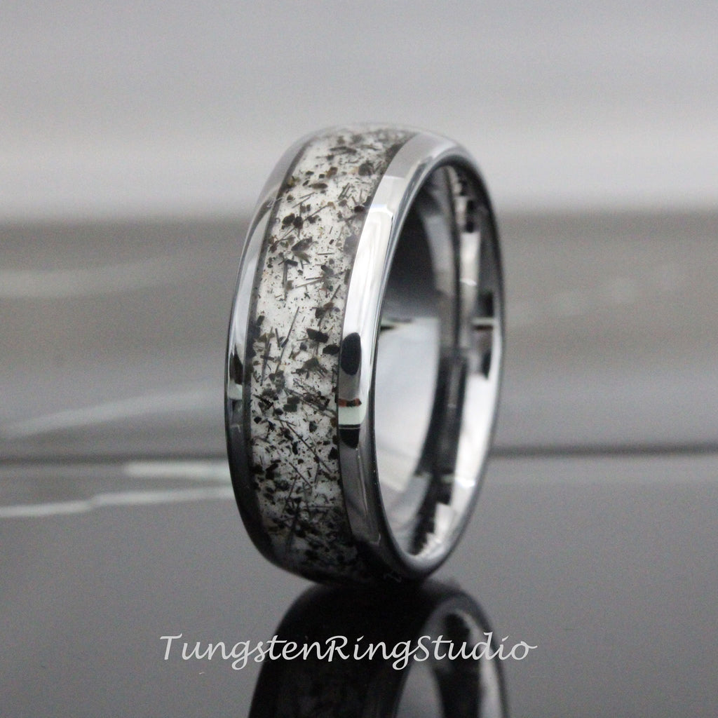 May include: A silver tungsten carbide ring with a black and white inlay. The inlay has a unique pattern of small black flecks on a white background.