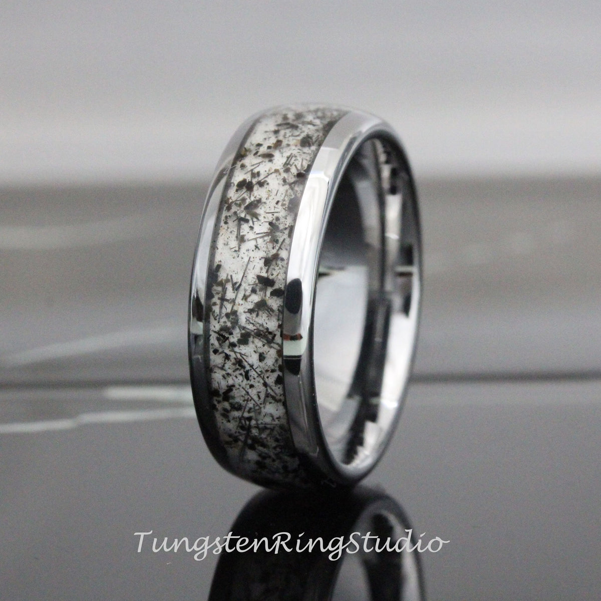 May include: A silver tungsten carbide ring with a black and white inlay. The inlay has a unique pattern of small black flecks on a white background.