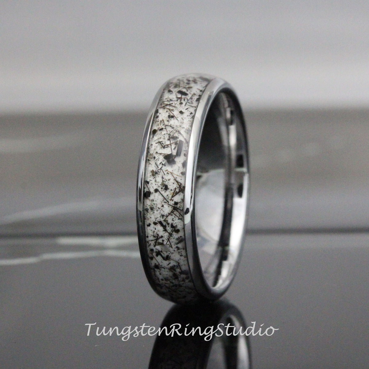 May include: A silver tungsten carbide ring with a white and black inlay. The inlay has a speckled pattern of black flecks.