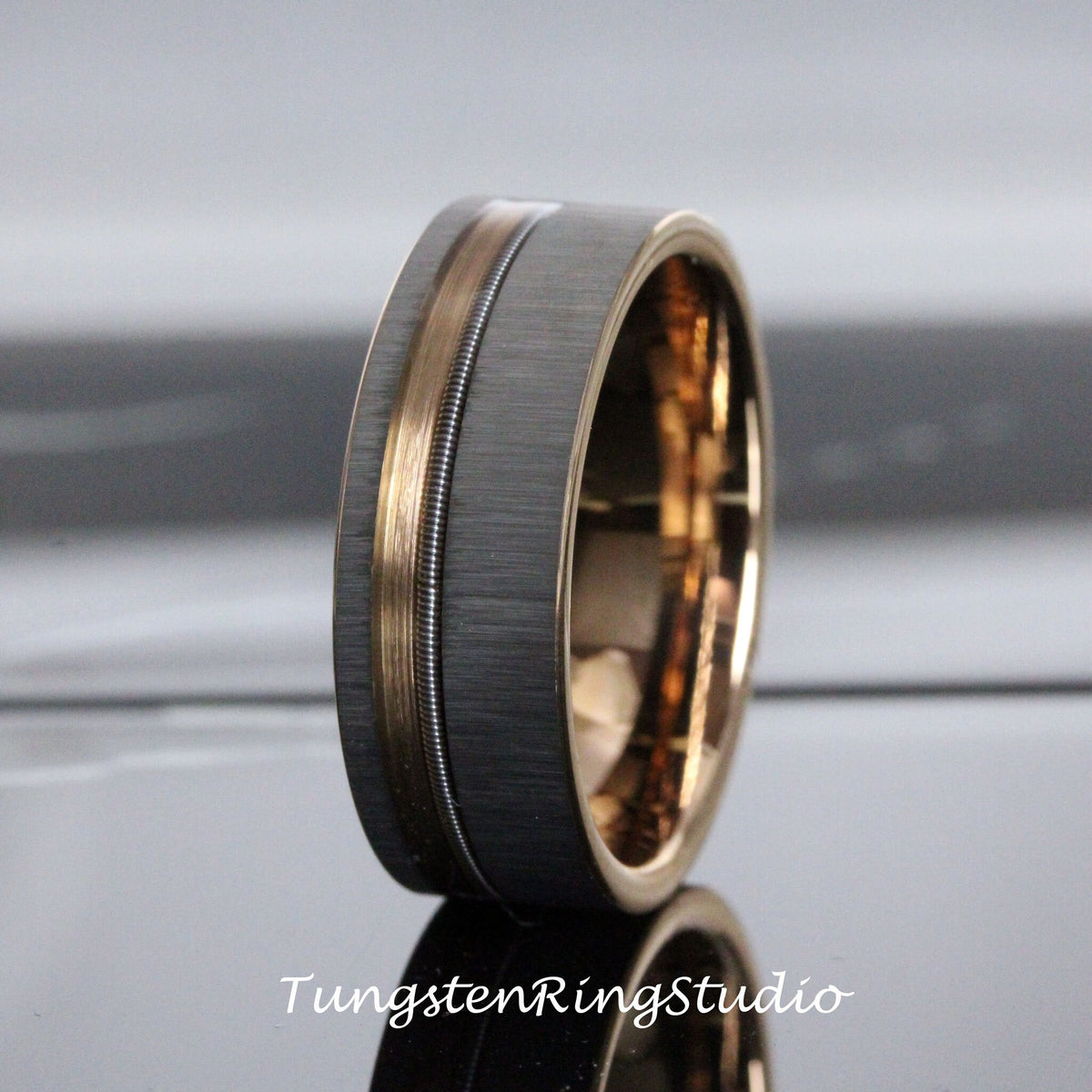 May include: A brushed black tungsten ring with a rose gold inlay and a silver groove. The ring is a classic style with a modern twist.