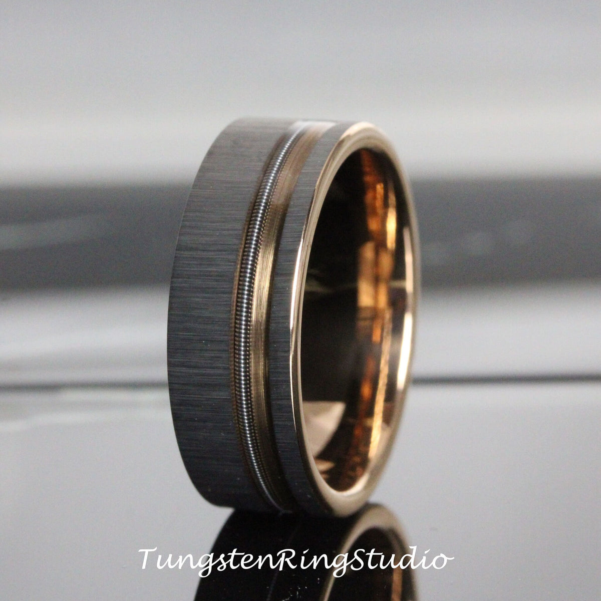May include: A brushed silver tungsten carbide ring with a rose gold inlay and two thin grooves. The ring is a classic style and is perfect for a wedding band or an engagement ring.