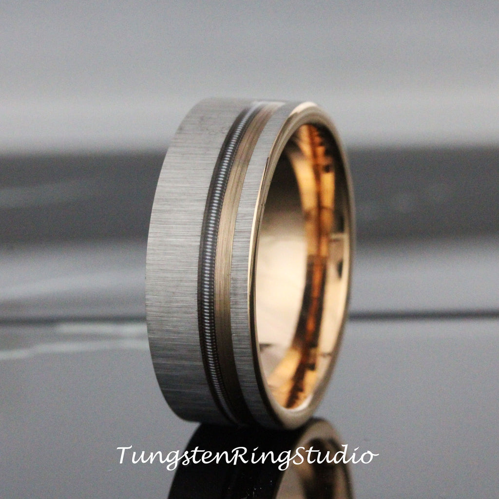May include: A silver tungsten ring with a rose gold inlay and a brushed finish. The ring has a grooved design around the inlay.
