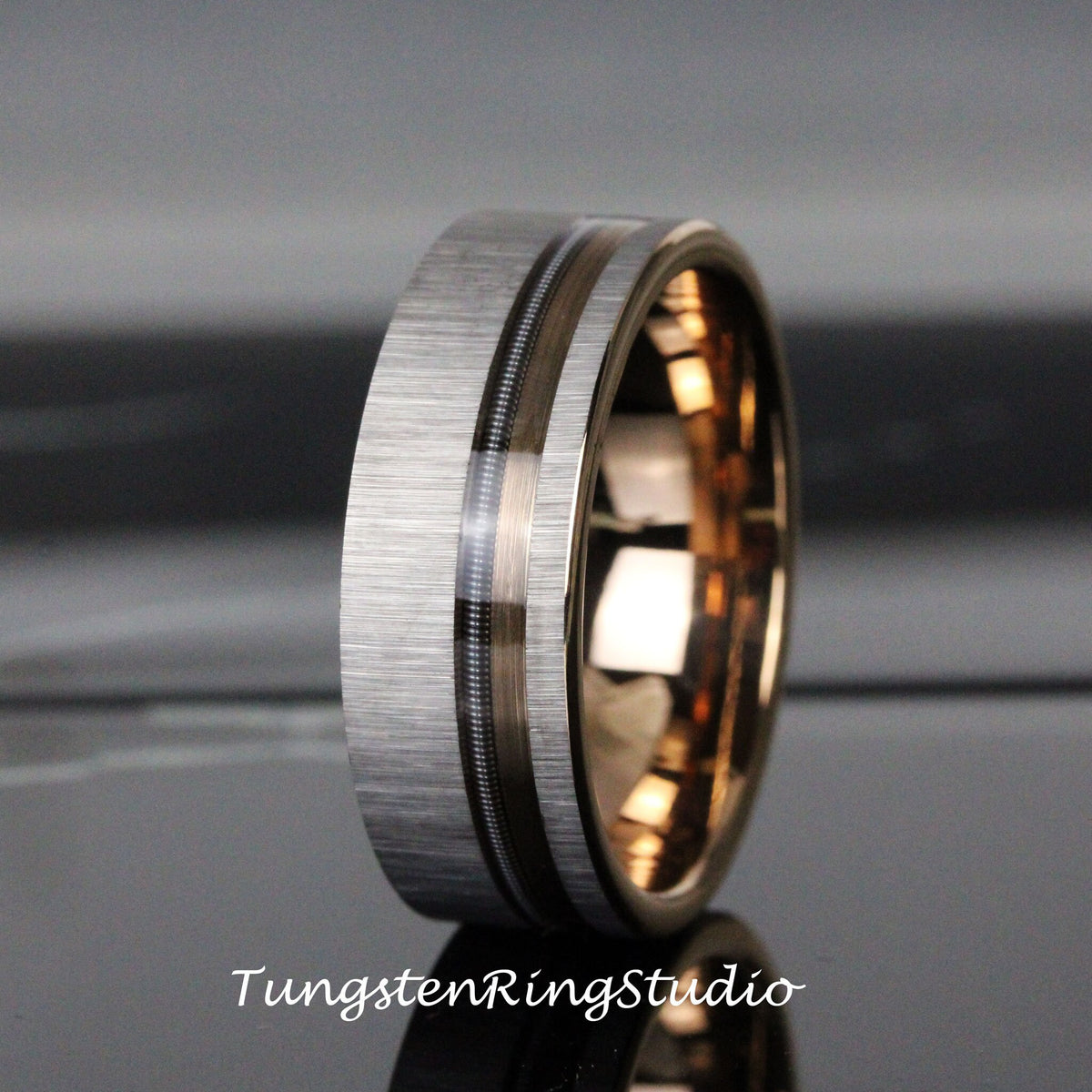 May include: A brushed silver tungsten carbide ring with a black and rose gold inlay. The ring has a beveled edge and a polished finish.