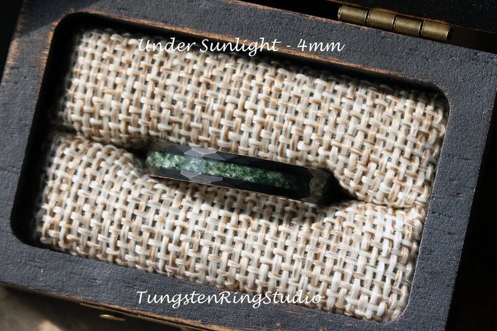 May include: A black tungsten carbide ring with a green inlay, displayed in a wooden box with a burlap lining. The ring is 4mm wide and the text "Under Sunlight - 4mm" is visible above the ring. The text "TungstenRingStudio" is visible below the ring.