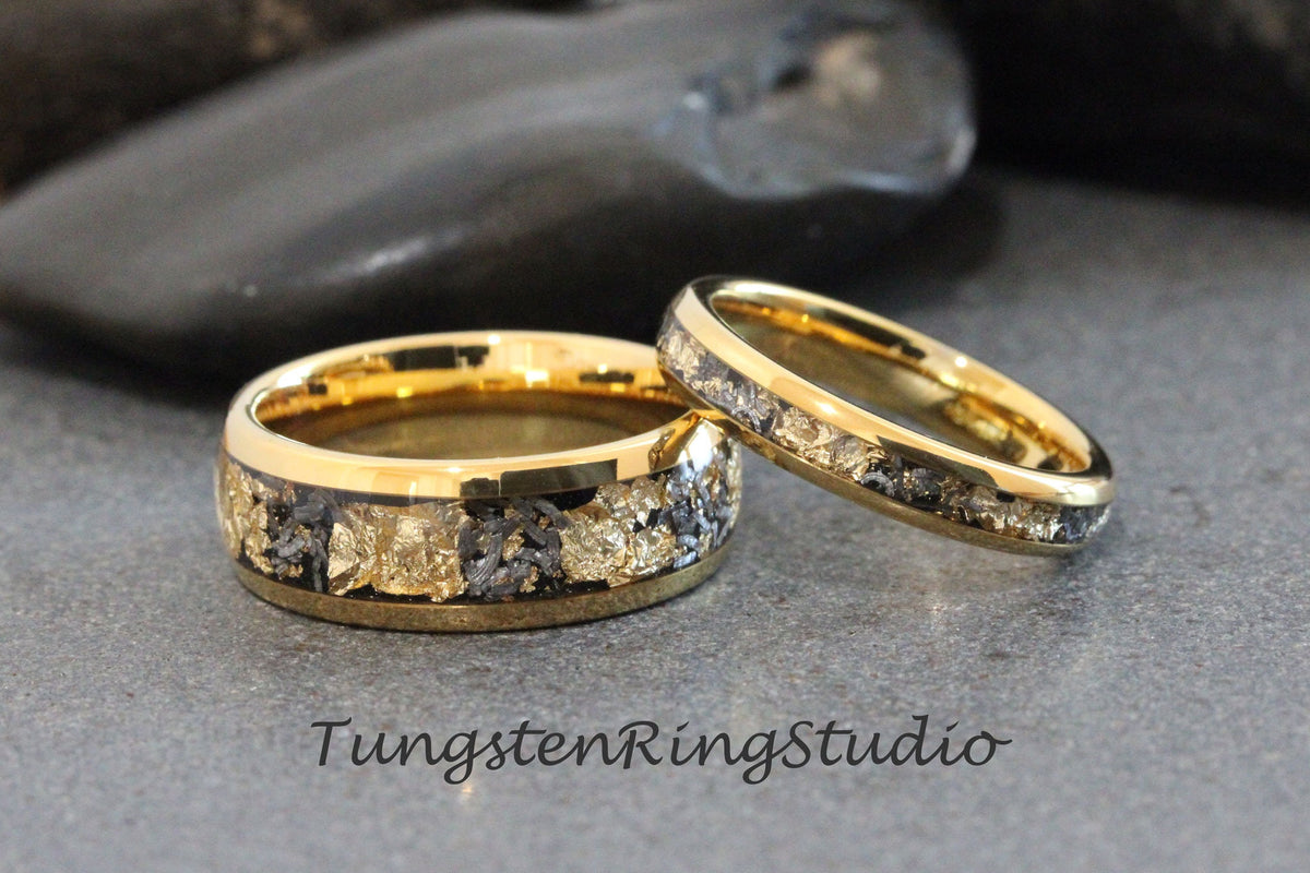May include: Two gold tungsten carbide wedding bands with a black and gold inlay. The bands are on a gray background.