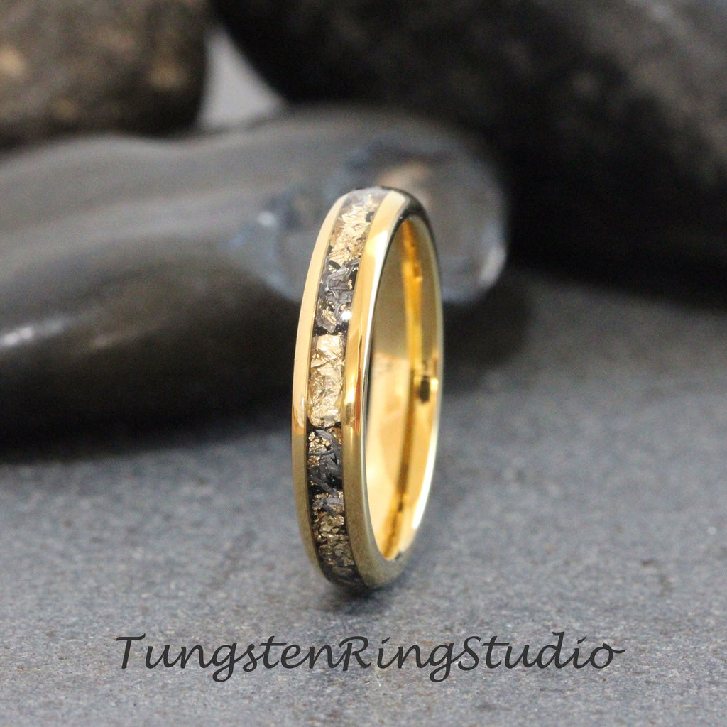 May include: A gold tungsten carbide ring with a band of black and white diamonds. The ring is a simple design with a polished finish.