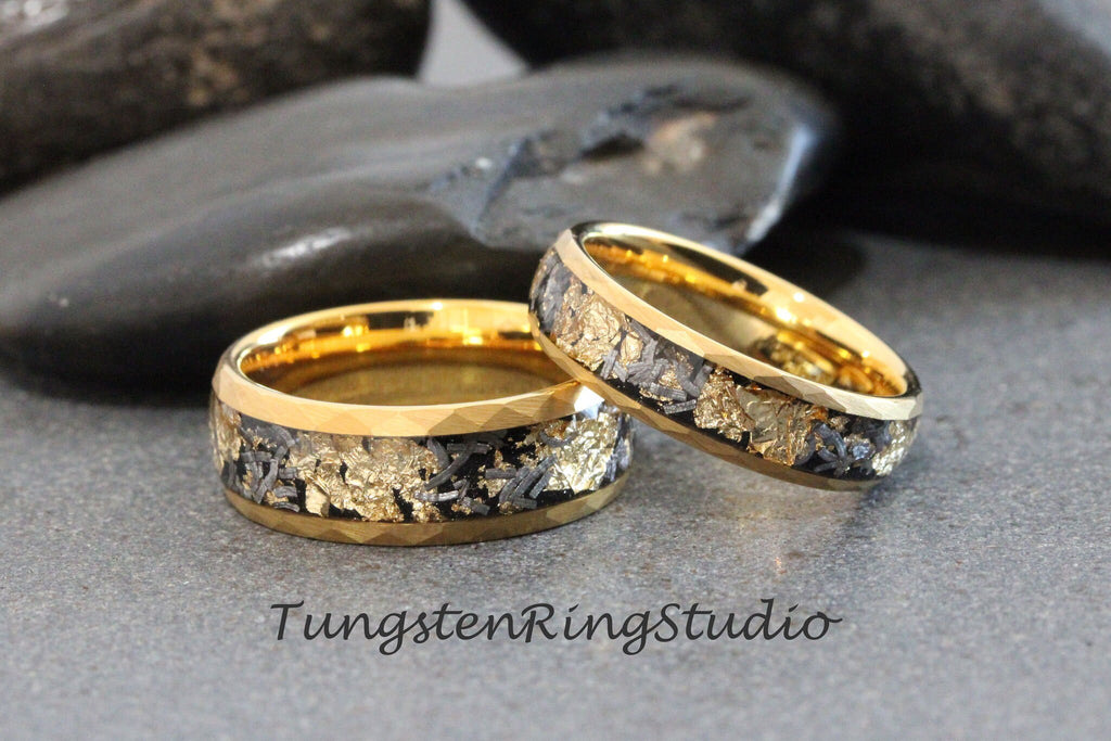 May include: Two gold tungsten carbide rings with a black and gold inlay. The rings are on a gray background.