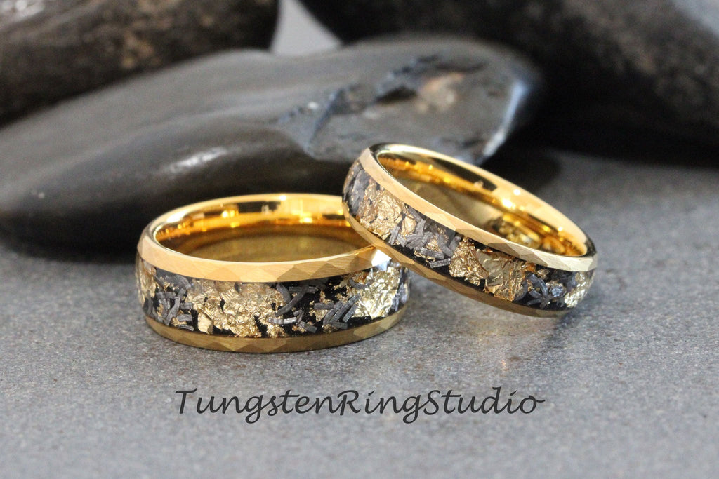 May include: Two gold tungsten carbide rings with a black and gold inlay. The rings are on a gray background.
