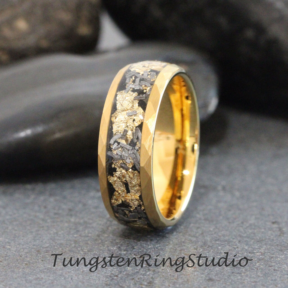 May include: A gold tungsten carbide ring with a black and gold inlay. The ring has a beveled edge and a polished finish.